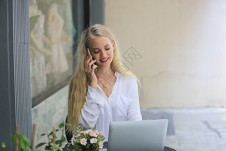 美丽的金发女郎在手机上讲话 笔记本电脑放在咖啡店外的桌子上自由职业者商务工作互联网技术工人人士工具细胞说话图片