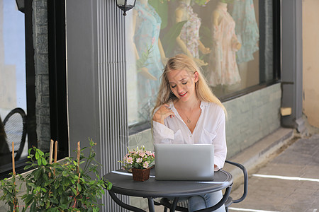 在零售店前拿着笔记本电脑坐着的美丽金发金发美女  小企业所有者概念技术自由职业者成人闲暇商务学习微笑女士女性互联网图片