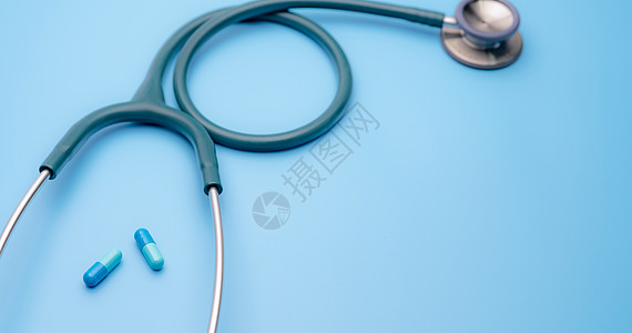 蓝色胶囊药丸和蓝色背景上的绿色听诊器 健康检查 用于心跳测试的心脏病学医生设备 医疗保健和医疗概念 用于诊断的诊断医疗工具卫生桌图片