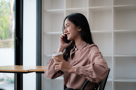 在一家咖啡馆 一位年轻漂亮的女士端着一杯咖啡正在打电话 为她的客户交谈和安排约会图片