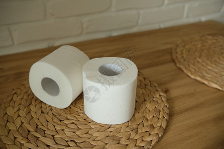 在一张木桌上的卫生纸 两个白卷 圆形编织垫 米色 白色砖墙背景地面屁股房子管子配件柔软度卫生洗手间家庭回收图片
