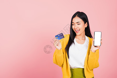 妇女笑着兴奋的微笑 手持手机和塑料借记信用卡快乐互联网电话信用银行购物女士姿势女性短信图片