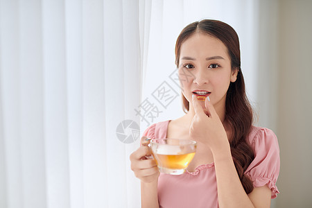 年轻美丽的亚洲妇女 吃药丸和饮用水饮食玻璃胶囊药品女孩医疗营养药店女性女士背景图片