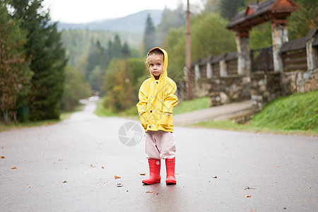 玩耍的女孩穿着黄色雨衣 同时在降雨时跳上水坑乐趣幸福淋浴天气快乐童年衣服孩子外套雨滴图片