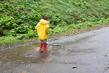 玩耍的女孩穿着黄色雨衣 同时在降雨时跳上水坑孩子外套季节快乐童年衣服乐趣雨滴幸福天气图片