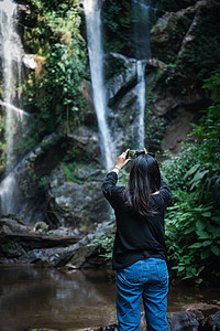 旅游女性在旅行度假时拍摄瀑布时很享受 亚洲女性放松户外探险旅游和休闲活动生活方式的后视图 假期户外旅行全景荒野岩石丛林拍照天堂热图片