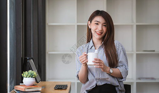 在咖啡店咖啡厅里喝咖啡和放松的亚洲妇女 与数字平板电脑合作时 美丽的女性在照相机上看镜头图片