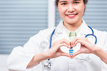 女医生微笑 用她的手印着心脏指尖 展示一小瓶科罗纳病毒疫苗的玻璃瓶图片