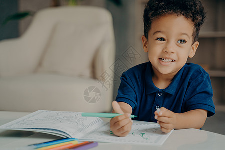 穿着深蓝色马球T恤的美国可爱小男孩 在家里画彩色书图片