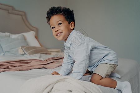 带着微笑的非裔美国人小孩 想爬上大床回家 在室内玩得开心图片