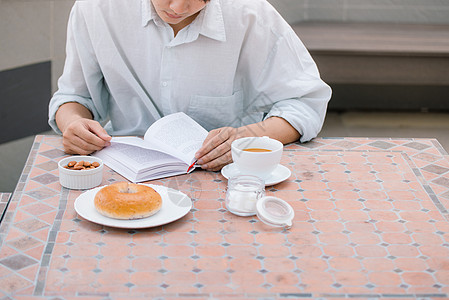 一个英俊男人的肖像 阅读一本书 享受他的咖啡早餐桌子房间成人白色男性面包杯子食物女士图片