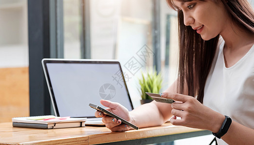 在线购物概念 年轻女性手持使用移动智能手机和信用卡在度假时使用桌上笔记本电脑进行在线支付图片