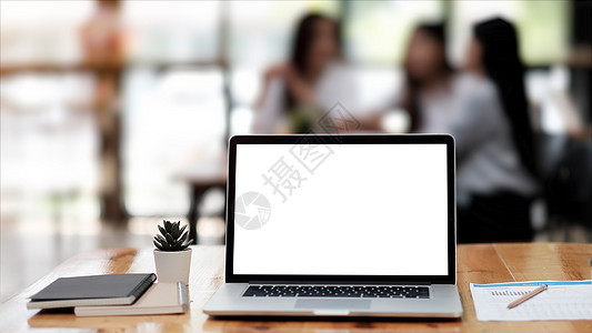 带白色空白屏幕的笔记本电脑照片放在现代工作台上 商务人士在后台开会模糊图片