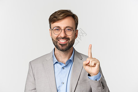 穿着眼镜和灰色西装的英俊长胡子男子近身露出一号 笑着微笑 站在白色背景上图片