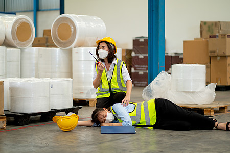 工厂女工使用对讲机寻求帮助 以支持和拯救在仓库工作区工作期间晕倒并躺在地板上的同事图片