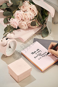 女人手里拿着笔 准备写 粉红玫瑰 笔和礼物 白色桌子上有粉红色的心 爱情观 圣瓦伦丁节的概念 母亲节的概念女性假期笔记本框架清单背景图片