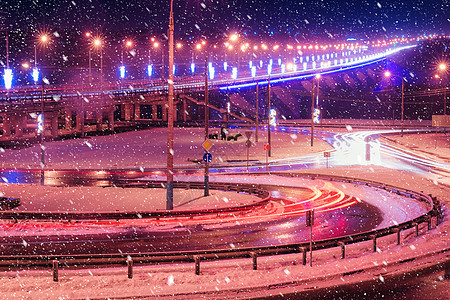 冬季晚上在大桥的雪瀑上行驶的汽车头灯的痕迹 湿沥青中的灯光反射景观交通辉光市中心城市大灯驾驶速度运动车辆图片