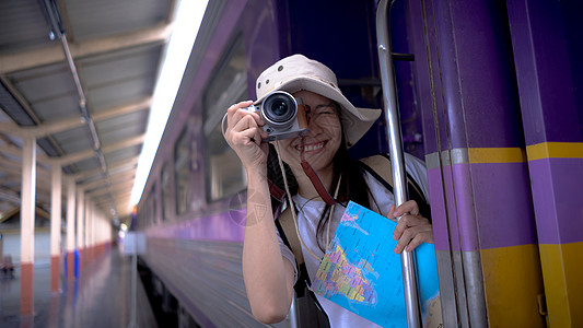 年轻的女游客在等火车旅行时微笑着用相机在火车上拍照旅游摄影 自由积极的生活方式概念图片