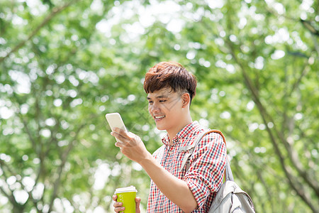 年轻的亚洲人微笑 在公园使用电话绿色手机音乐咖啡成人男性学生潮人长椅图片