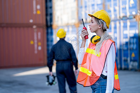 工头或货运集装箱女工使用对讲机与她的团队和同事技术人员在后台进行交流图片