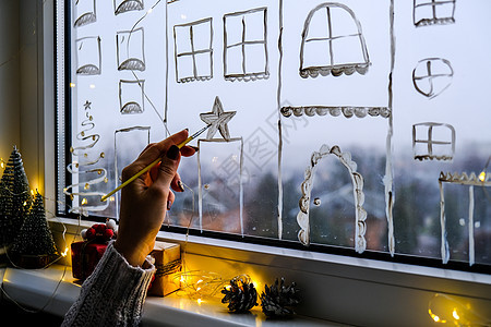 女手在窗户玻璃上画圣诞假期装饰 新年风景 城市建筑花环灯 Hygge 装饰和圣诞节概念风格店铺传统女性雪片湿气庆典假期花环展示图片