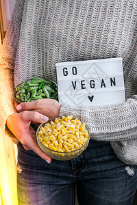 女人们手中有带短信的灯盒GO VEGAN 韦加大信教 素食健康生活方式 冷冻碗中的食品 绿豆和黄玉米图片