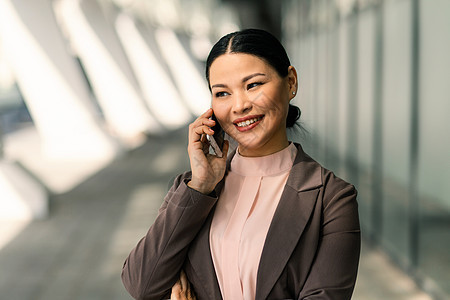 在商务中心的背景下 身着西装 面带微笑的亚洲女商务人士在手机上交谈 高质量照片图片