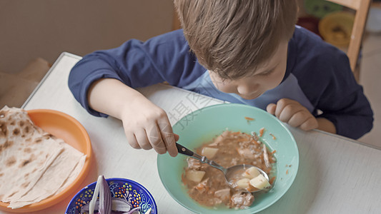 饥饿的男孩坐在吃汤桌旁图片