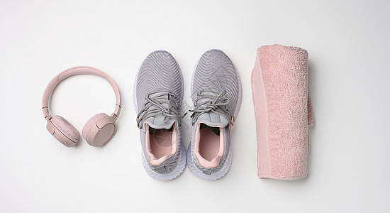 两对灰色纺织运动鞋 无线耳机和白色背景的粉红色毛巾 用于运动 跑步粉色运动装音乐鞋类技术配件衣服工具活动女性图片