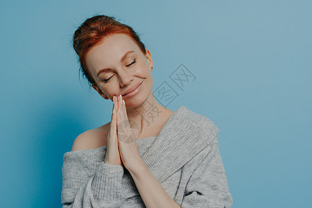 快乐的平静的红发女心怀感激的女士 在工作室用闭着眼睛握手祷告图片