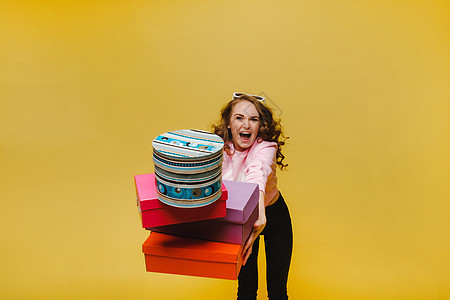 一个快乐的年轻女子 在以橙色工作室背景孤立地购物后 带着彩色纸盒 季节性销售 购买 花钱买礼物购物中心女士微笑市场乐趣店铺购物狂图片