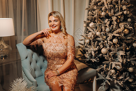 一个穿着晚礼服的女孩坐在 圣诞树附近的沙发上新年幸福头发喜悦乐趣女士女性化裙子红色奢华图片