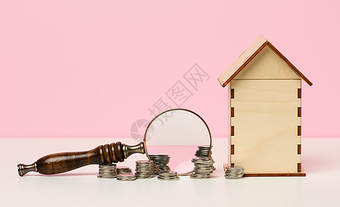 粉红色背景的金属货币和放大镜及木屋 B 不动产租金 (单位 美元)图片