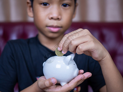 男孩在白猪存钱罐里存钱 储蓄的概念 为未来储蓄钱盒快乐商业推杆投资孩子情感男性微笑童年图片