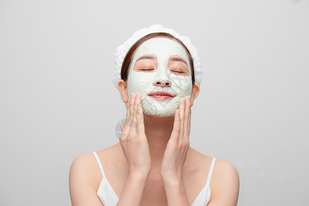 满意女人的长相改善了皮肤状况 戴着面罩 用白色背景触摸脸颊和脸部清洁女士治疗黏土健康面具温泉女性沙龙化妆品图片