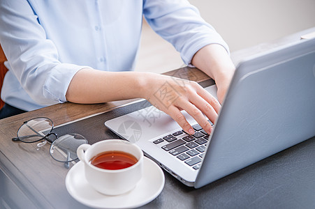 商业概念 穿蓝衬衫的女士在电脑上打字 办公室桌上有咖啡 背光 太阳光亮效应 特写 侧视图 复制空间商务键盘写作衬衫人士职场女孩蓝图片