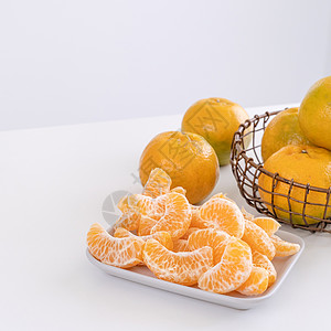 盘子里漂亮的去皮橘子和金属篮子 在现代现代厨房岛的明亮白色干净桌子上隔开食物果汁热带月球水果橙子摄影图片