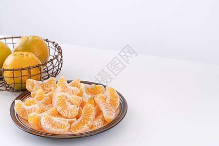 盘子里漂亮的去皮橘子和金属篮子 在现代现代厨房岛的明亮白色干净桌子上隔开果汁热带月球水果食物摄影服务橙子图片