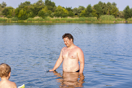 在一个非常炎热的夏日 一家人 一位父亲和他的儿子们正在河里游泳 在水库游泳 一个幸福的家庭在夏天玩得开心 在水中嬉戏笑声水池池塘图片