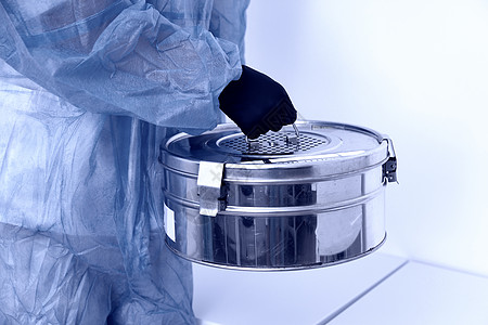 实验室里站着的人拿着带防护服的自动板压消毒器金属盒 蓝色拖鞋图片