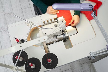 在车间工作室使用专业超锁缝制缝纫机的青年妇女 以上是裁缝店装配 缝衣或缝合服装的设备图片
