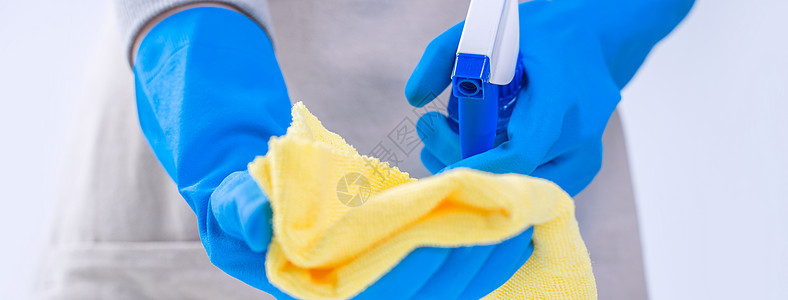 年轻女管家正在用蓝手套 喷雾清洁剂 湿黄色抹布 闭合 复制空间 空白设计概念在围裙内打扫白桌女士守门员工人办公室桌子洗涤剂卫生蓝背景图片