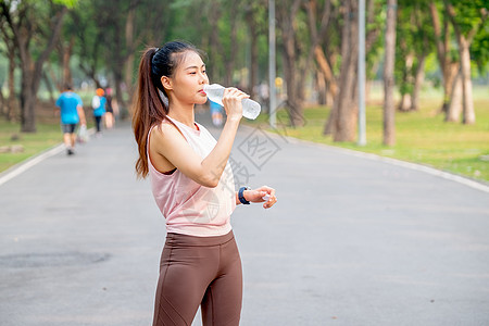 亚洲女性穿着粉红色运动服站在公园的路上 清晨锻炼时喝瓶装水 在早上练习时图片