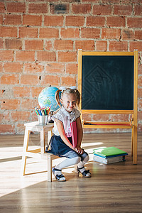 穿着校服的小可爱女孩坐在黑板旁边 拿着一本书图片