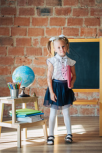 身着校服的可爱小女孩 穿着校服 坐在有书本的校董会旁边图片