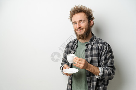 微笑的帅哥 卷发和胡须喝着咖啡杯 穿着白色背景中突显的格子长袖衬衫成人咖啡店男人快乐杯子商务休息饮料闲暇咖啡图片