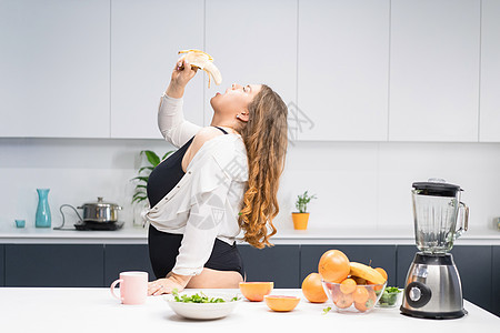 女孩坐在厨房的桌子上 尝试节食的年轻胖女人 饮食年轻胖女人站在厨房里 特写胖乎乎的女性降低 BMI 重量 尝试快速减肥的健康食品图片