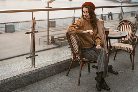 等待或沮丧的法国年轻女子坐在户外街边的餐馆里 看起来很沮丧 户外穿着秋衣和红色贝雷帽的时尚年轻女性肖像微笑城市店铺食物女孩餐厅成图片