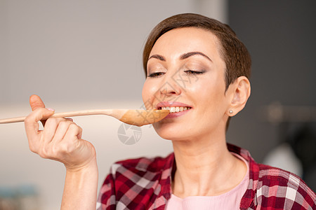 一位女士使用长木勺尝试烹制菜肴的特写镜头 站在新房子的现代厨房里 留着短发的女人为家人做晚餐 家里的健康食品水果女性桌子女孩乐趣图片