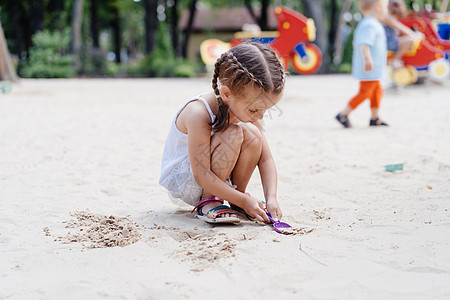 玩沙箱游戏的小女孩 在挖掘沙沙沙幕建筑沙沙图夏季日喜悦乐趣沙坑公园女孩太阳童年女儿幸福玩具图片